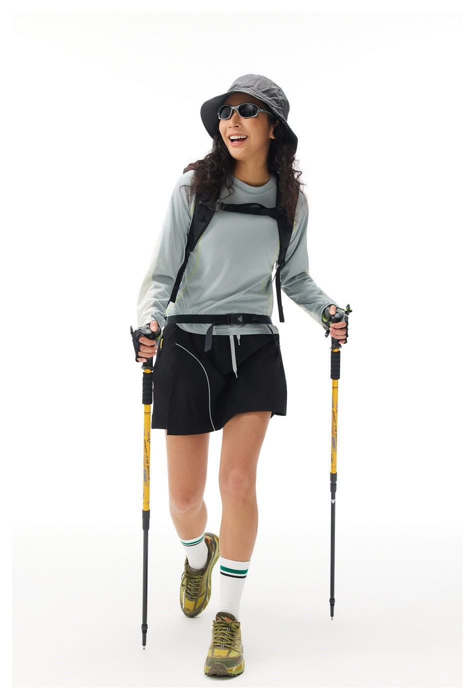 Model wearing a pale gray long-sleeve top with lime seams and a black skort, shown from the front while hiking.