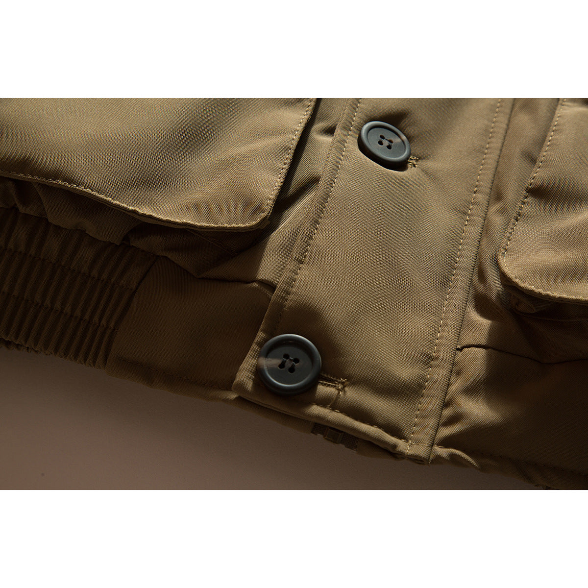 Close-up of a tan jacket's button placket, pocket edges, and ribbed hem.