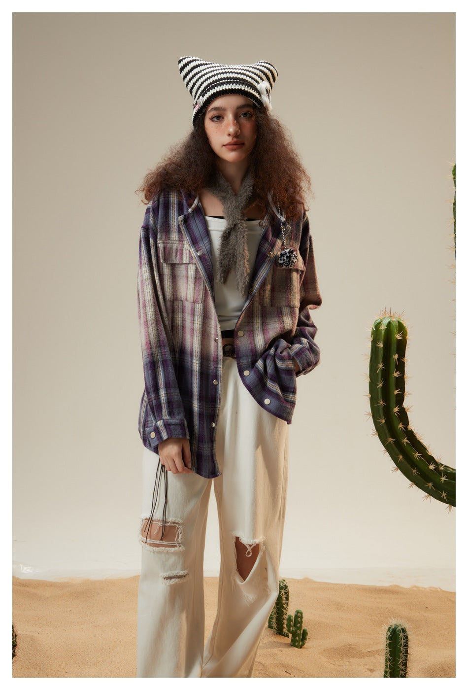 Full-length model in an open purple plaid jacket and white trousers, wearing a black-and-white striped knit hat.