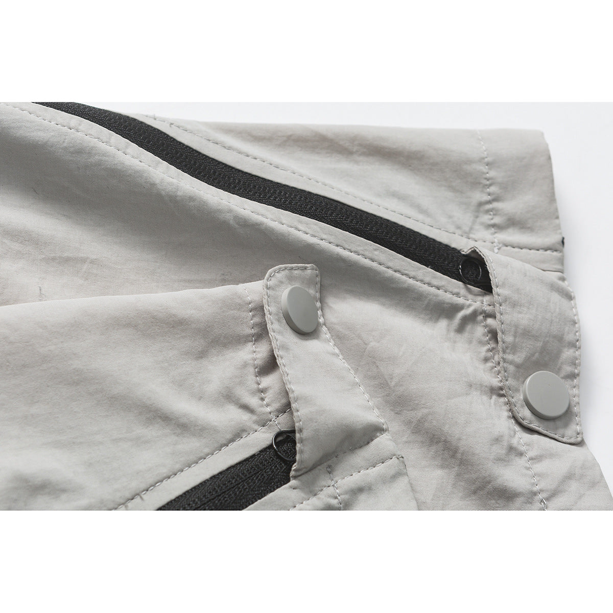 Close-up of light gray trousers with black zipper trim and pale snap-button tabs.