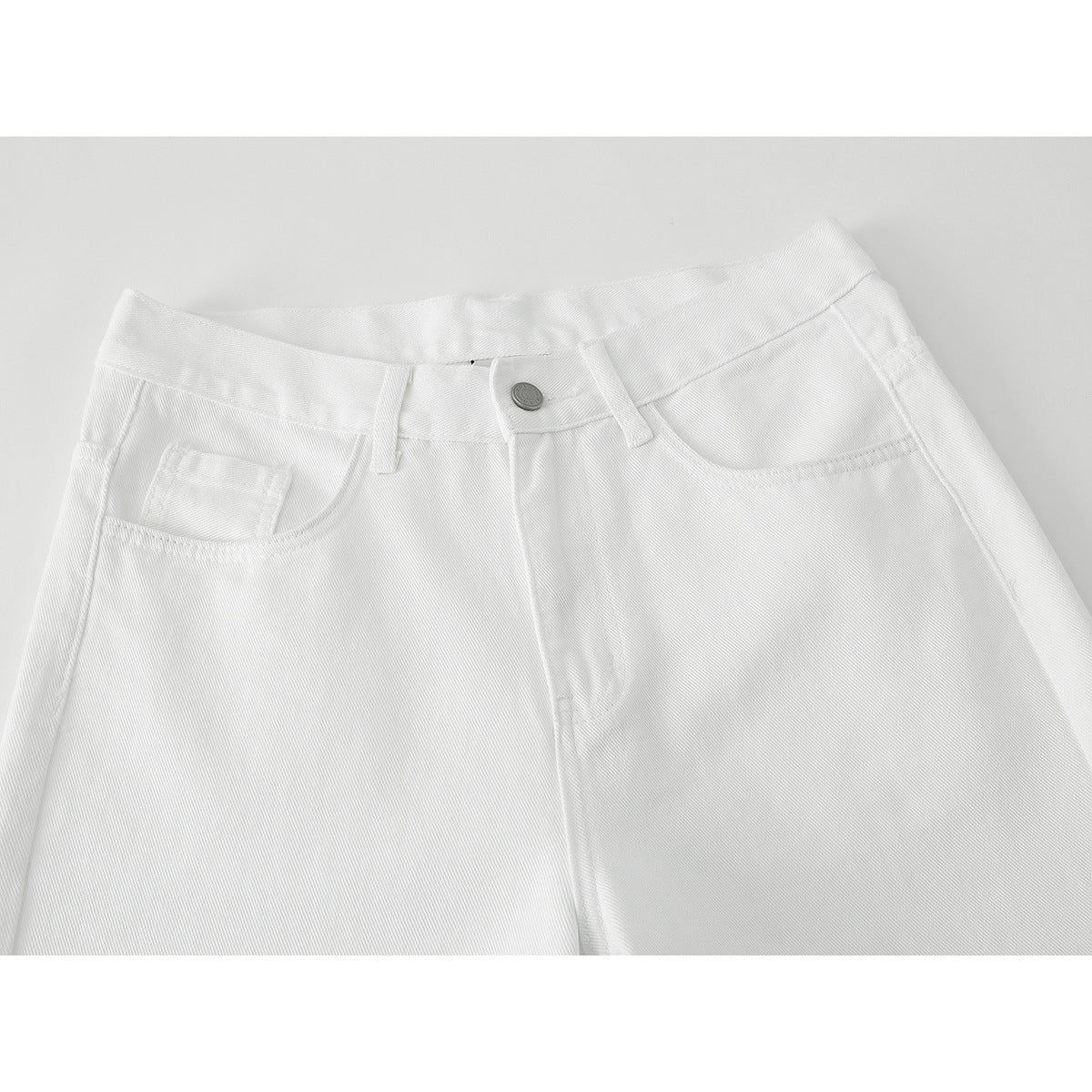 Close-up of white wide-leg pants showing the front waistband, button, belt loops, and pockets.