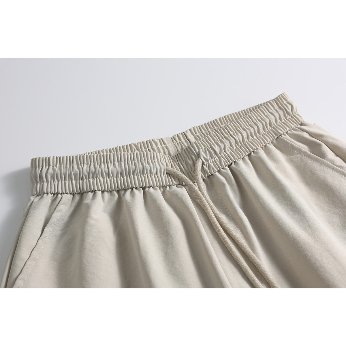 Close-up of beige shorts showing the gathered elastic waistband, drawstring, and pocket stitching.