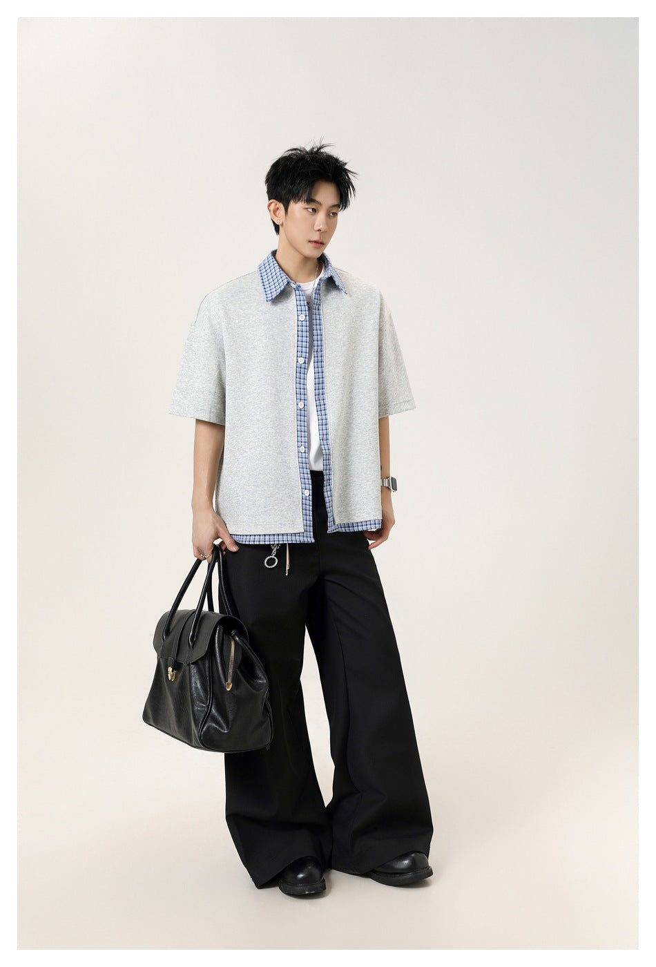 Model wearing a light gray short-sleeve button-up shirt with blue plaid trim, paired with black trousers.