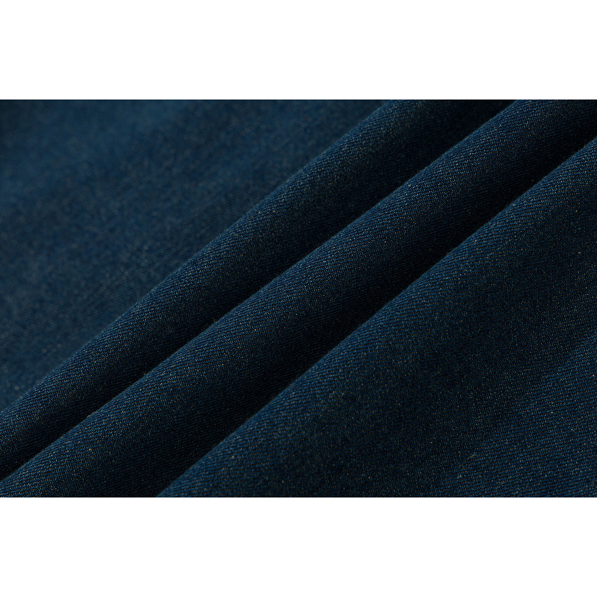 Macro view of dark indigo denim fabric folded into soft ridges.