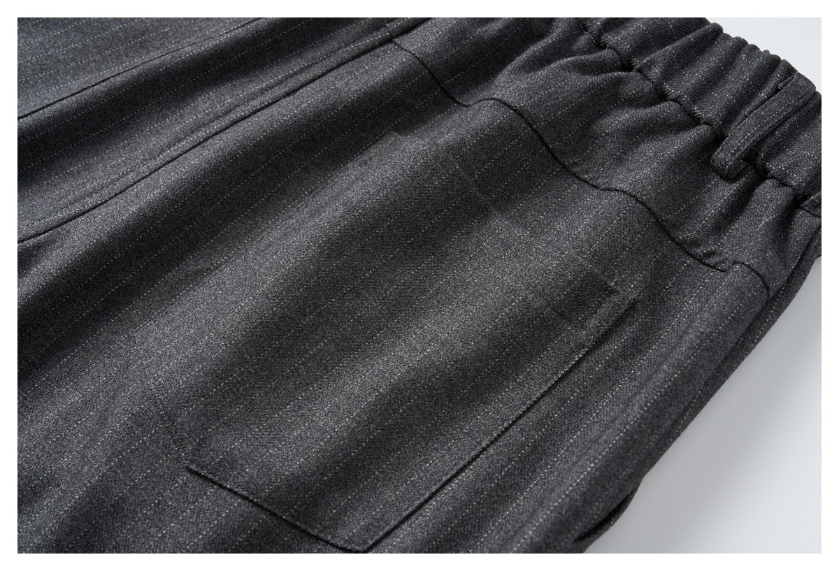 Close-up of charcoal trousers showing a stitched pocket, front seams, and elastic waistband with belt loops.