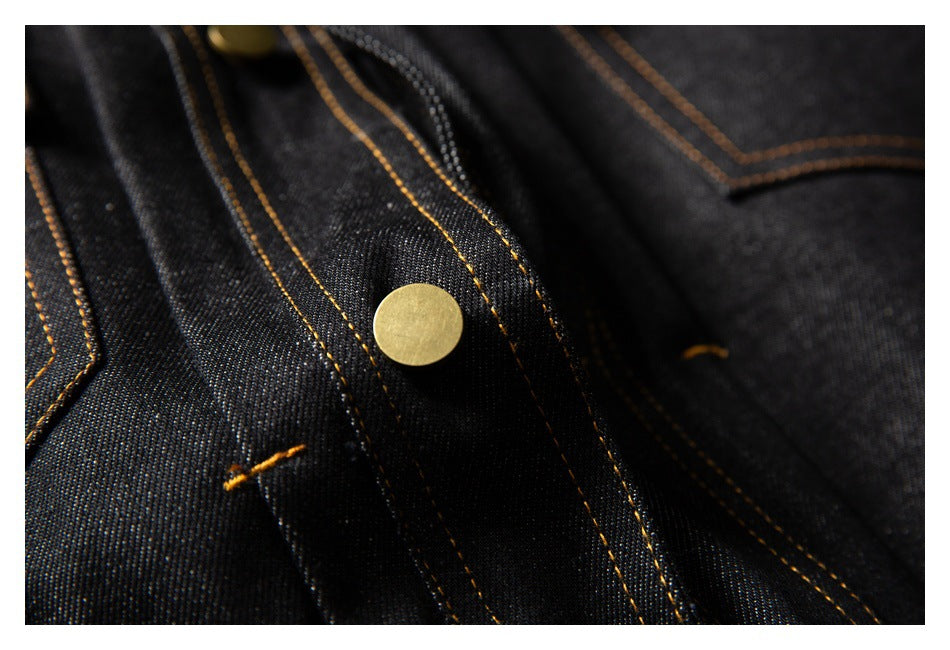Close-up of black denim with a brass-colored button and contrasting golden stitching.