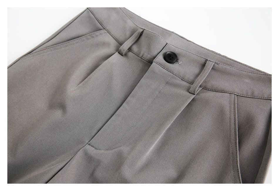 Close-up of gray trousers showing the waistband, button, belt loops, fly, and front pocket.