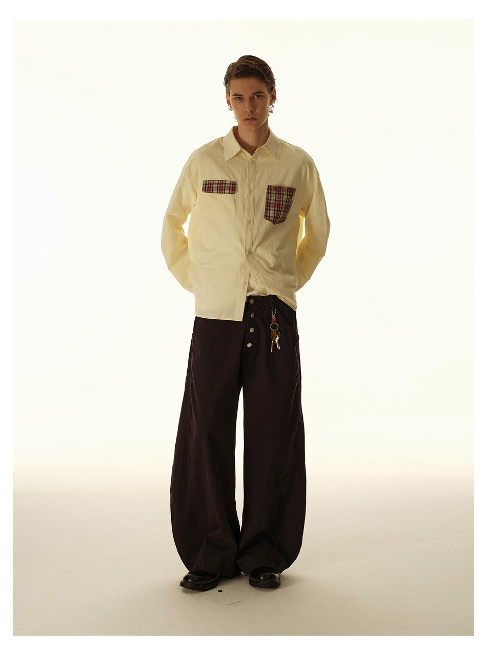 Full-length model wearing a cream button-up shirt with plaid chest pockets and wide dark trousers.