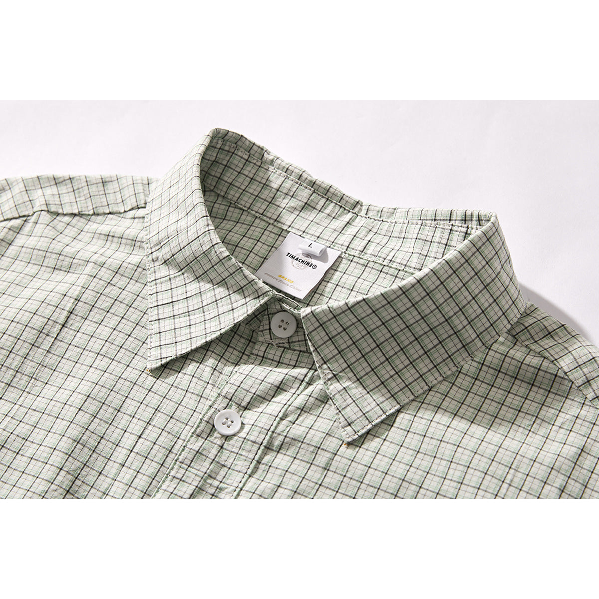 Close-up of a pale green and gray plaid shirt collar, white buttons, and inner neck label.