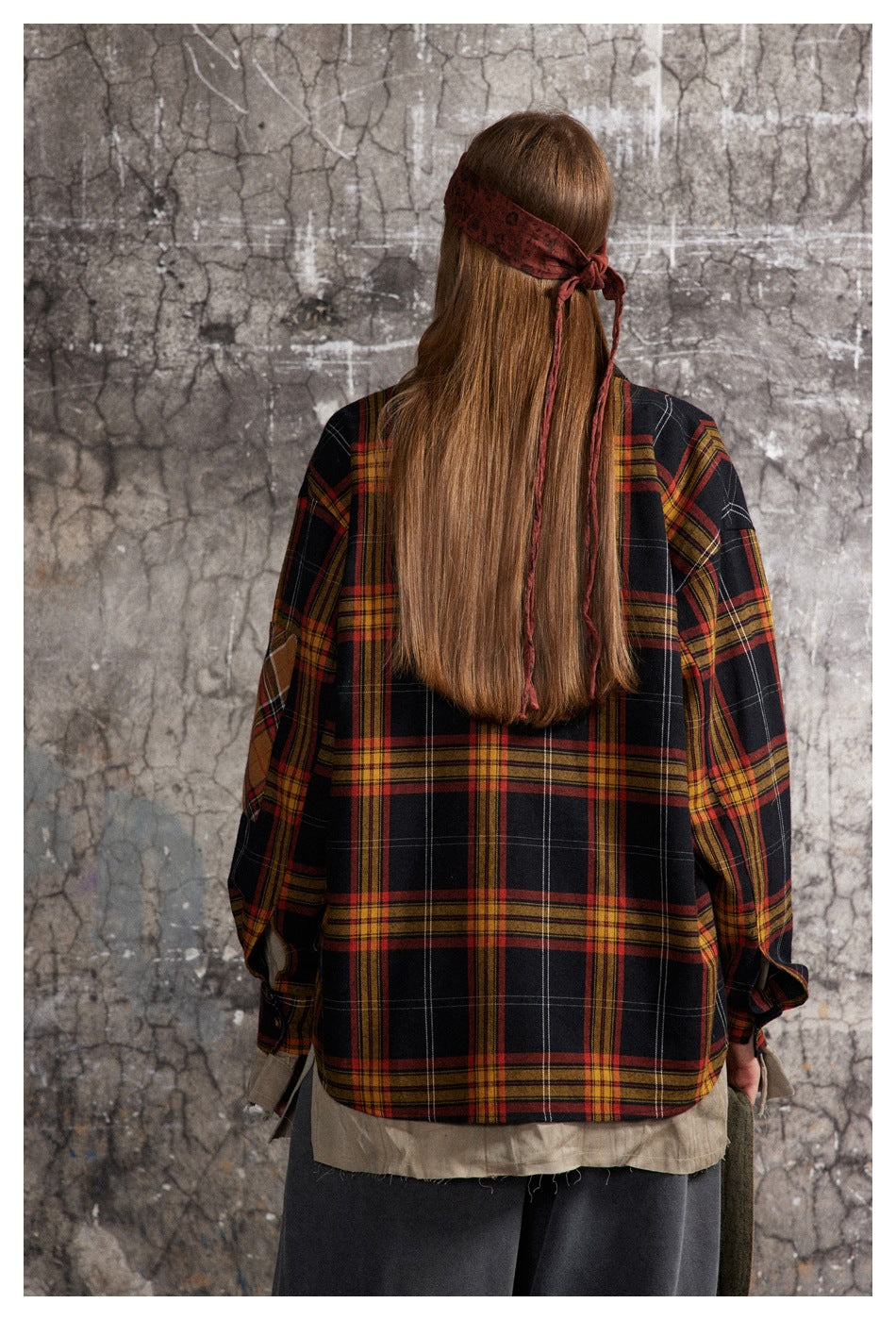 Back view of a model wearing an oversized black plaid shirt with red and mustard stripes and contrasting sleeve patches.