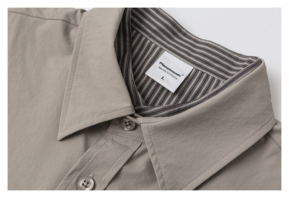 Close-up of a taupe shirt's pointed collar, buttons, and striped inner collar.