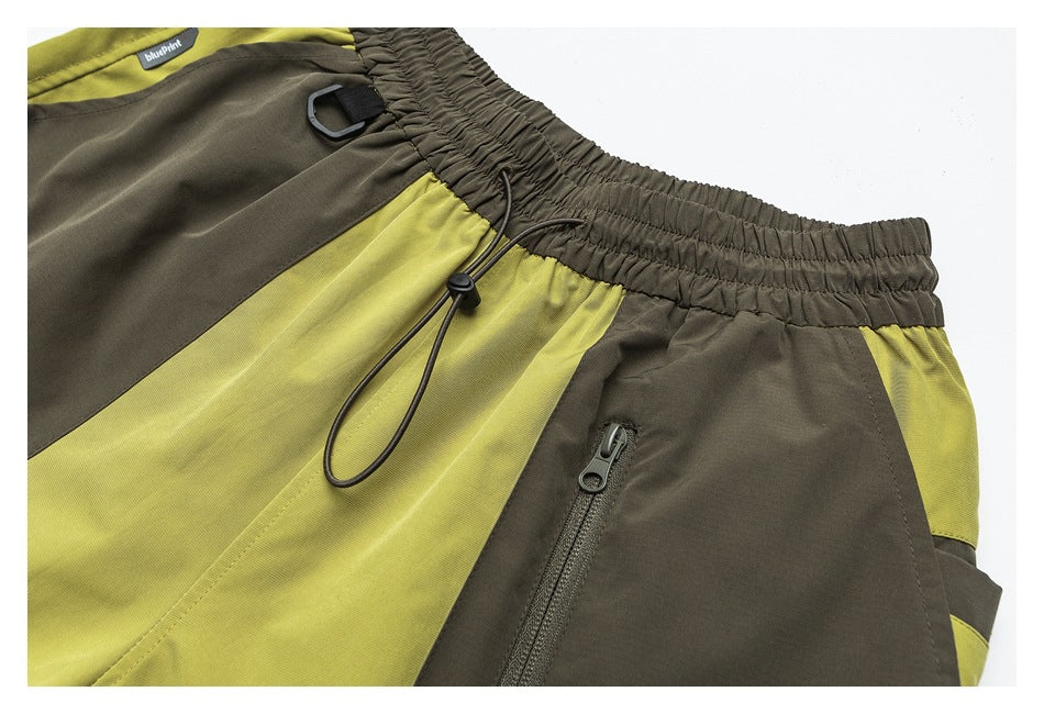 Close-up of olive and chartreuse color-block shorts showing the elastic waistband, drawcord and zip pocket.