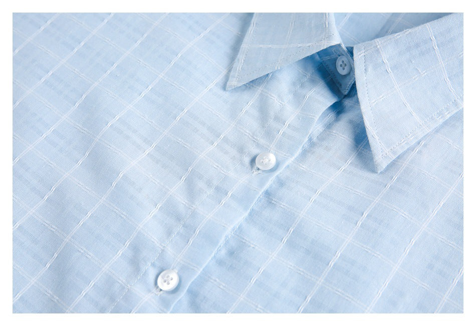 Close-up of a pale blue shirt collar, white buttons, and white windowpane stitching.