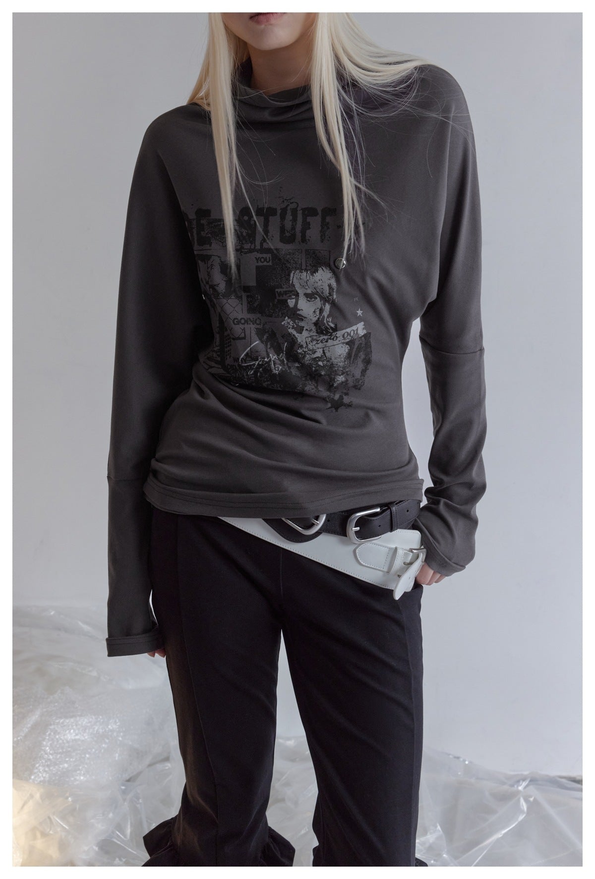 Model wearing a charcoal long-sleeve draped-neck top with a dark front graphic and black trousers.