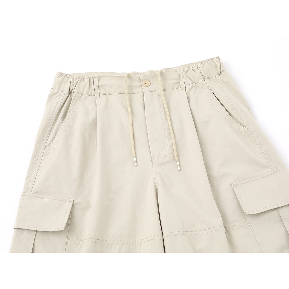 Close-up of light beige cargo pants showing the elasticized waistband, drawstring, front pockets and flap cargo pockets.
