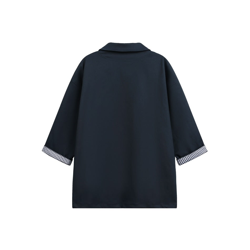 Back view of a navy collared shirt with checked fabric visible at the turned-back sleeve cuffs.