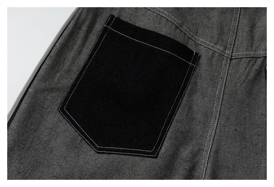 Close-up of a black patch pocket with contrasting stitching on gray trousers.