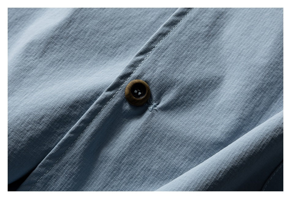 Close-up of a dark button and stitched placket on light blue fabric.