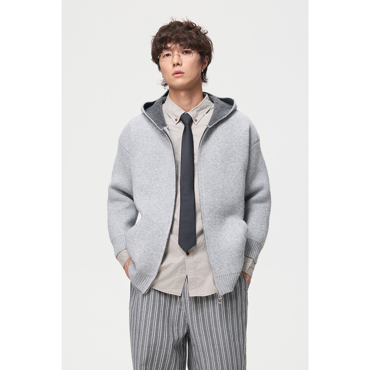 Model wearing a light gray hooded knit jacket with a front zipper, layered over a shirt and tie.