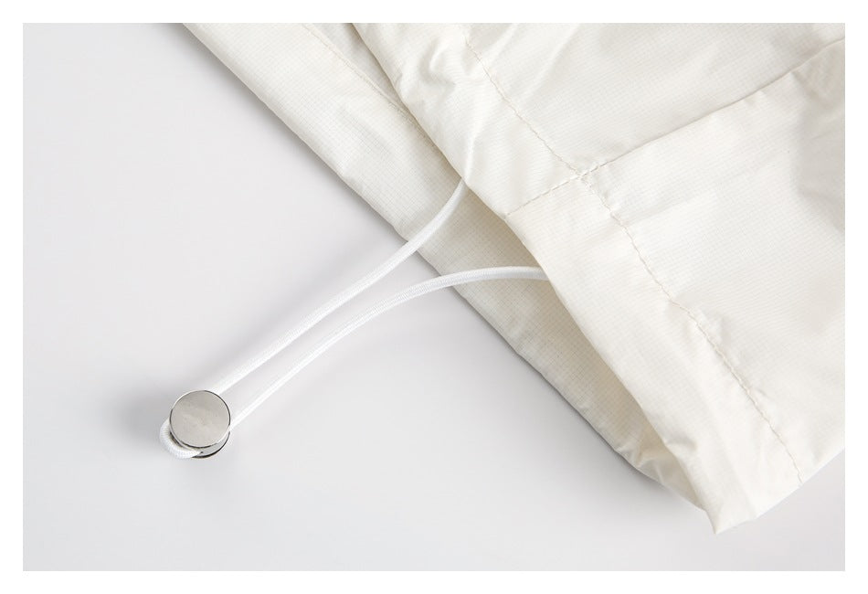 Close-up of a white drawcord with a round metal toggle beside an off-white garment hem.