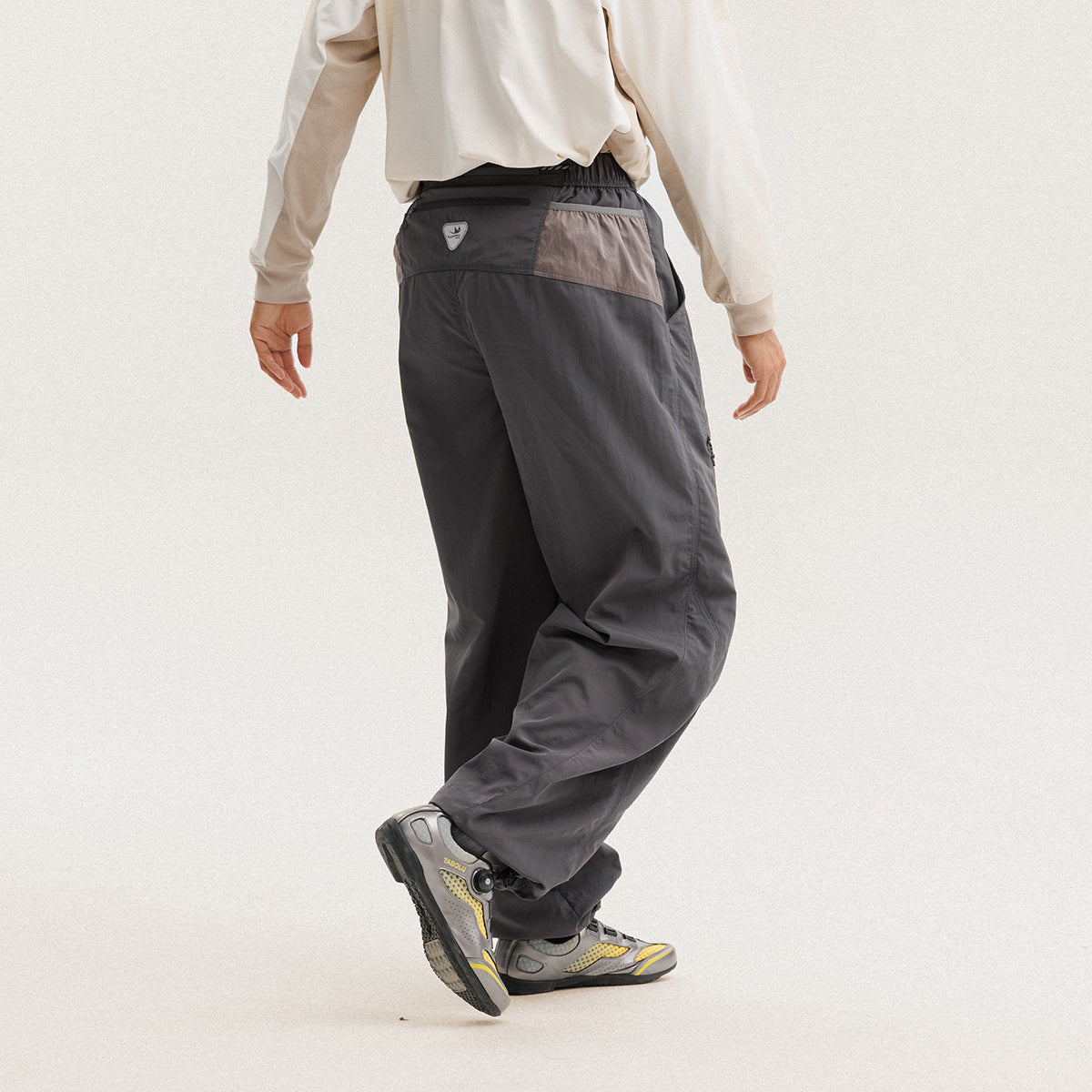 Rear view of a model wearing loose charcoal-gray pants with a contrasting taupe back panel.