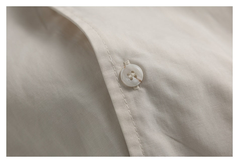 Close-up of a translucent four-hole button sewn onto pale beige fabric.