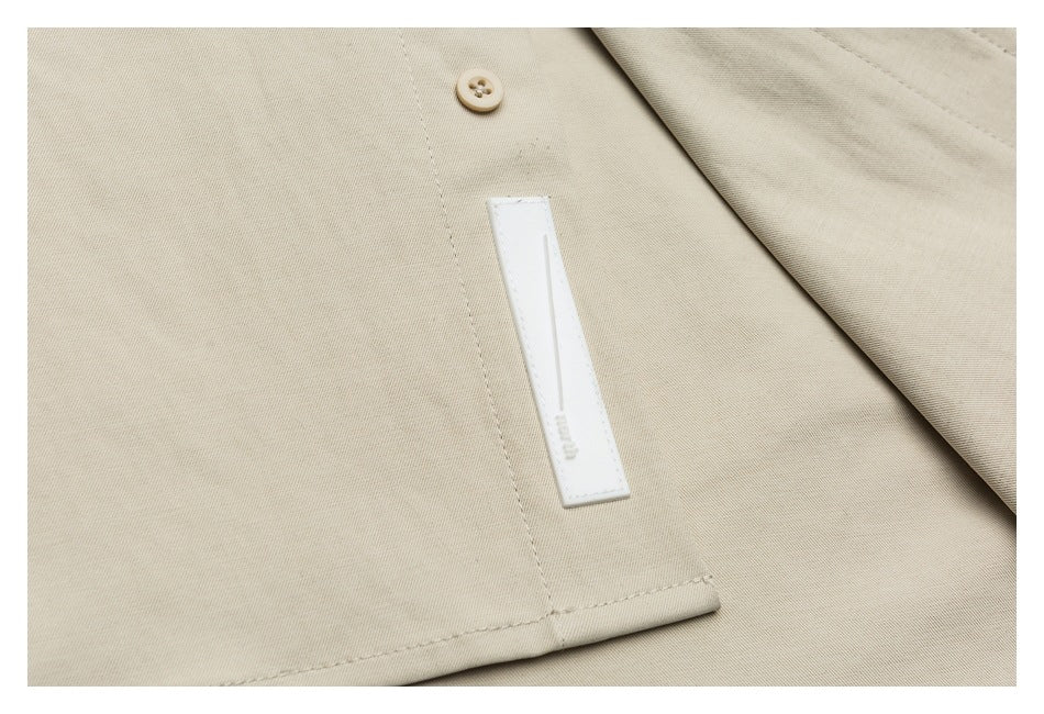 Close-up of beige garment fabric with a tan button, stitched hem, and a narrow white sewn-on label.