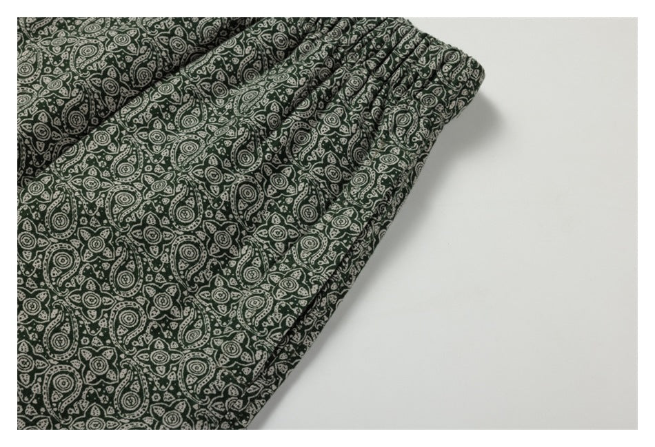 Close-up of the gathered waistband and front seam on dark green paisley-print pants.