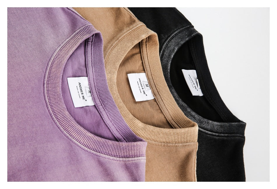 Close-up of the ribbed collars and sewn labels on purple, tan-brown, and black T-shirts.