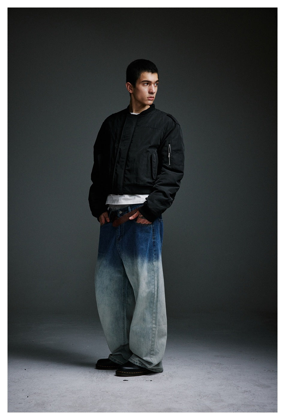 Three-quarter view of a model wearing a black bomber jacket and very wide blue jeans with pale washed legs.