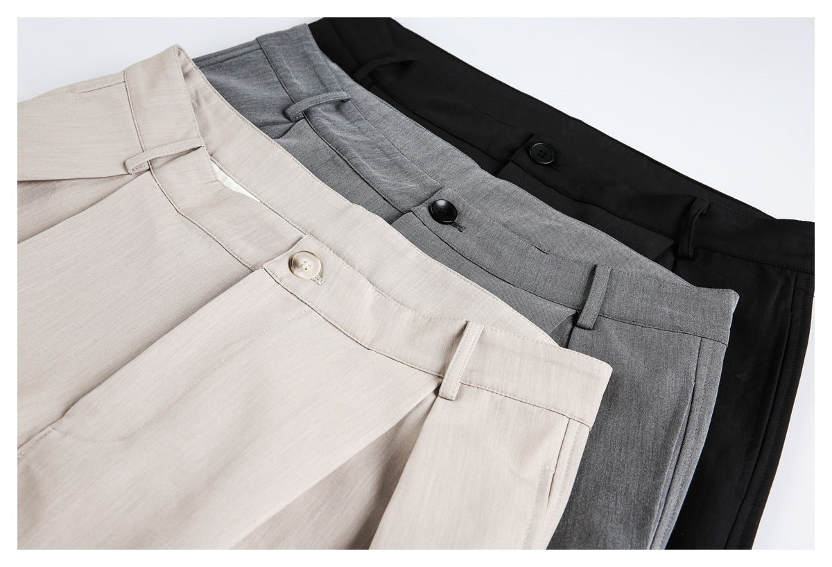 Close-up of beige, gray, and black trousers arranged together, showing waistbands, buttons, and belt loops.