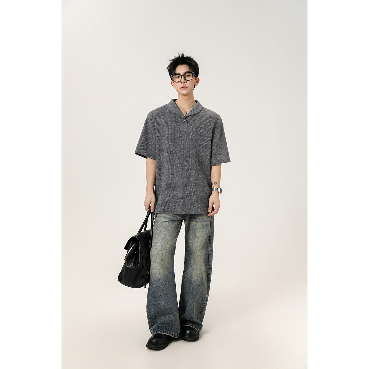 Full-length model wearing a loose gray short-sleeve knit polo shirt with wide-leg faded jeans.