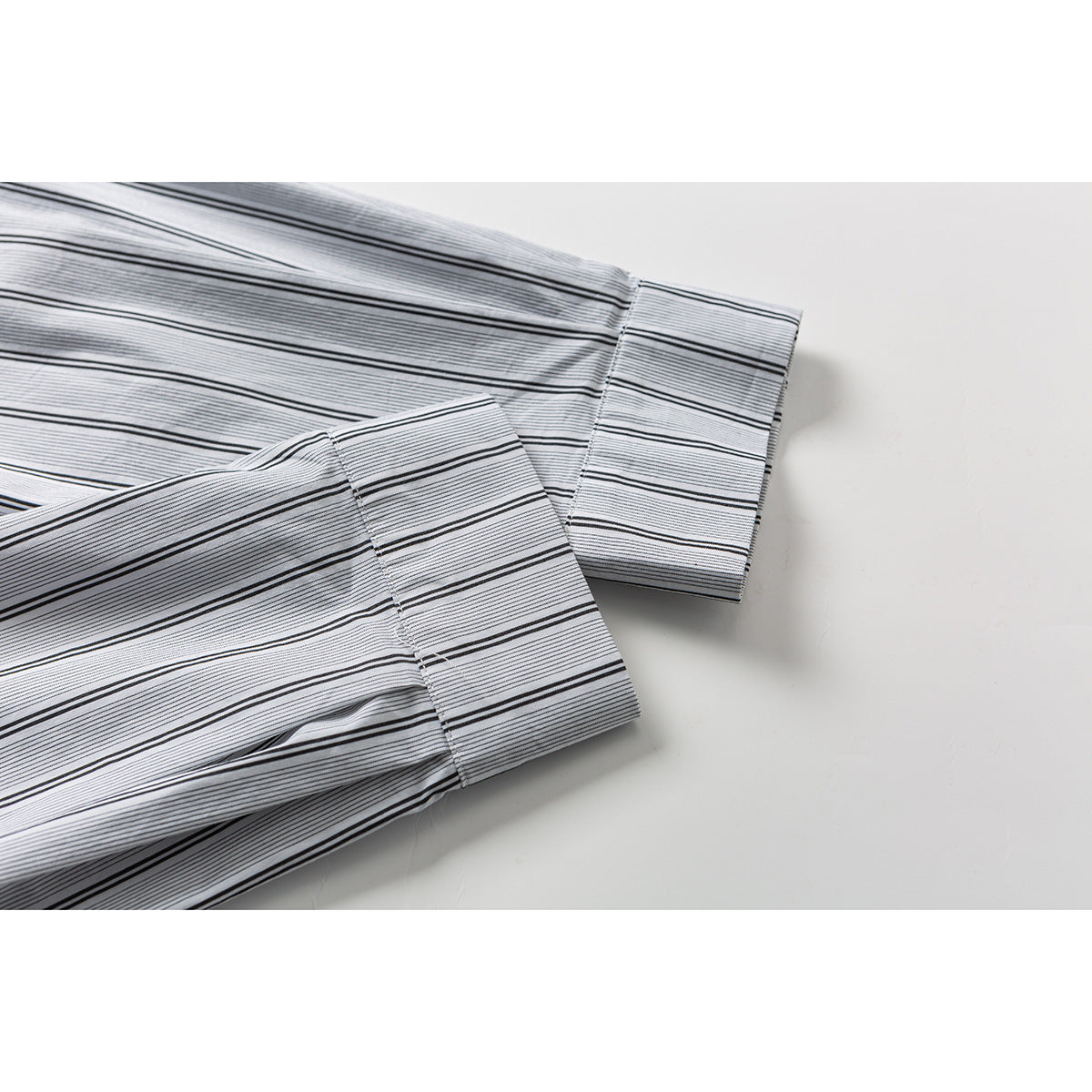 Close-up of two long sleeve cuffs on a white shirt with fine black stripes and wider black lines.