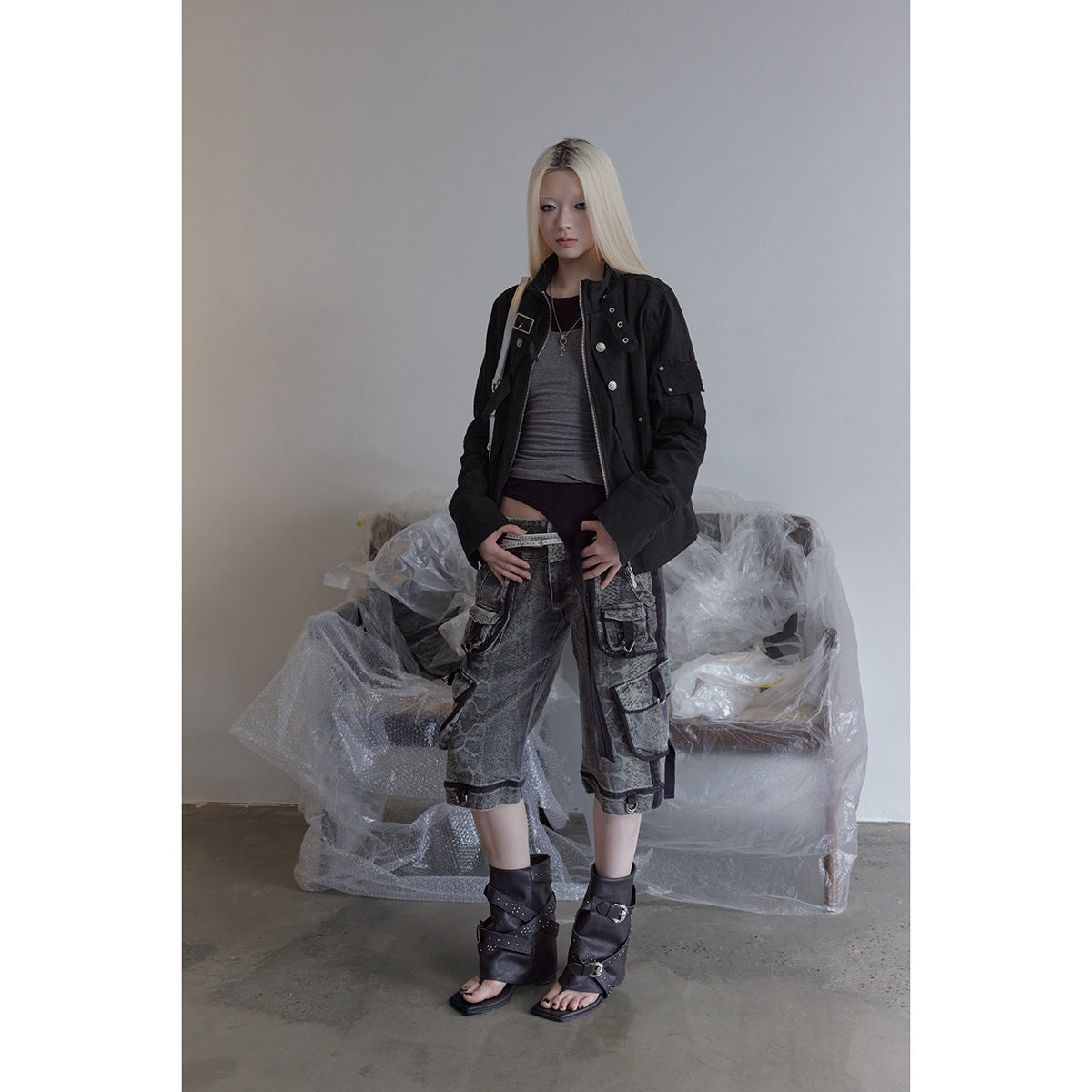 Model wearing a black utility jacket, gray patterned cargo shorts, and black buckle sandals.