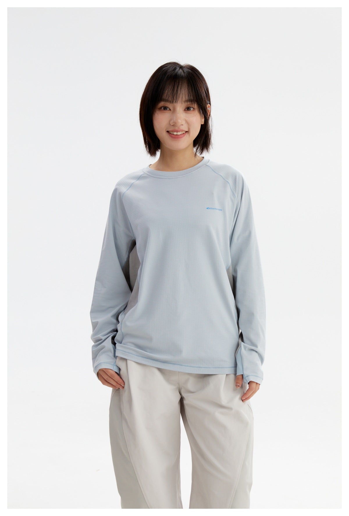 Model wearing a pale blue long-sleeve shirt with gray side panels and white trousers, shown from the front.