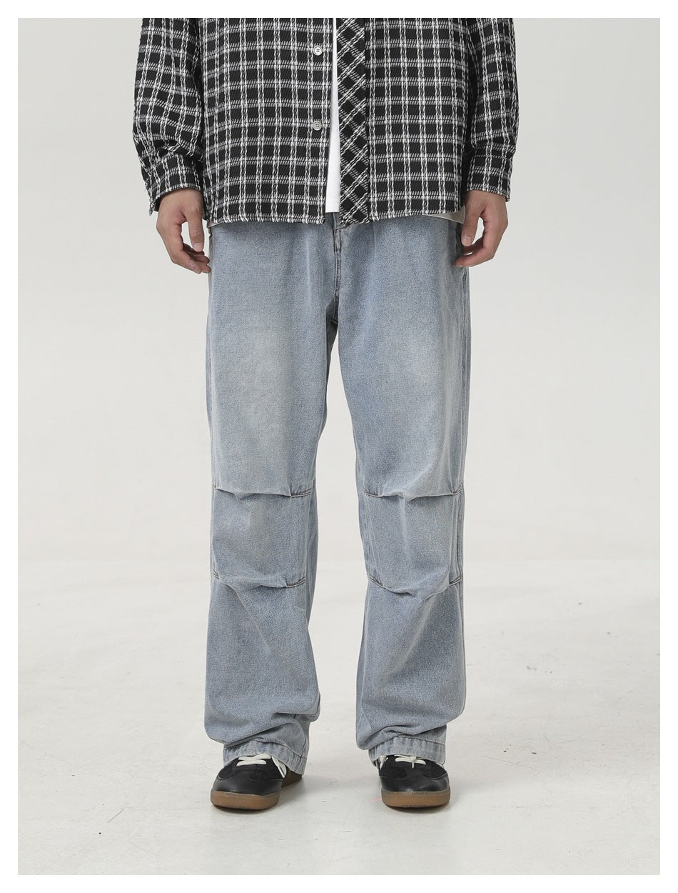 Person wearing light-blue wide-leg jeans with knee pleats, a plaid shirt and black sneakers, front view