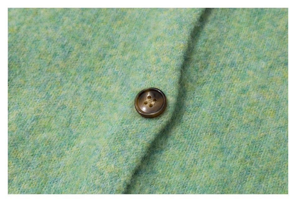 Close-up of a brown four-hole button on mottled mint-green and yellow knit fabric.