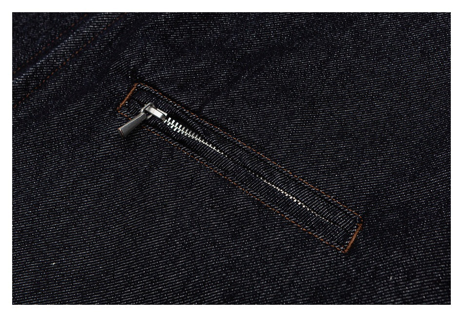 Close-up of a silver zipper on a dark indigo denim jacket pocket with contrasting orange stitching.