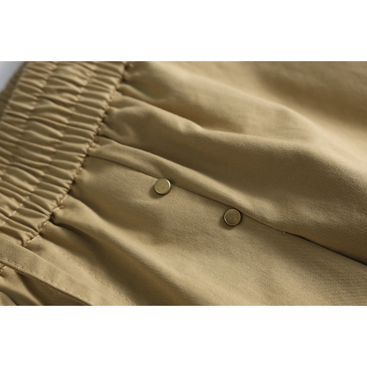 Close-up of tan shorts with a gathered waistband, textured fabric and two small metal buttons.