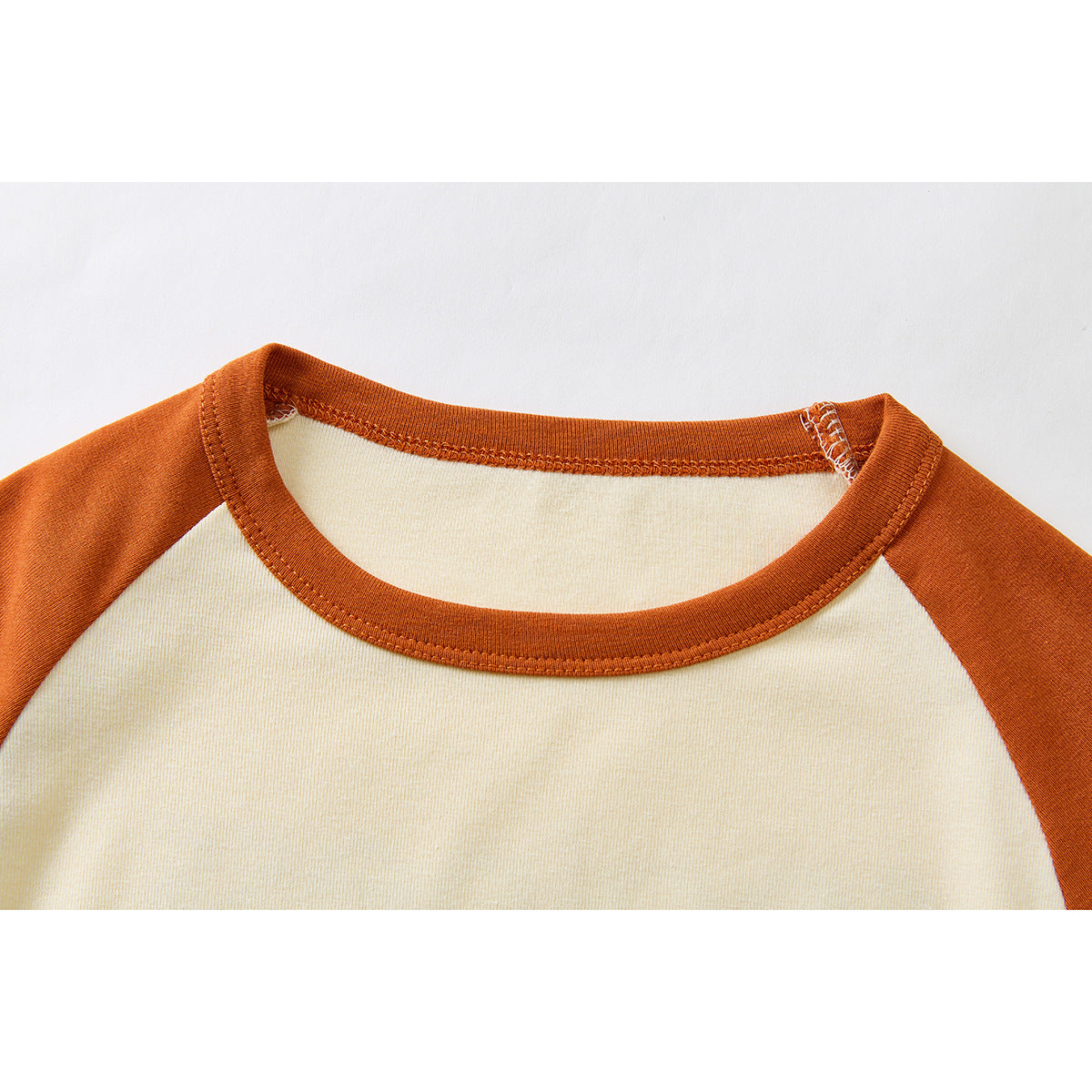 Close-up of the cream shirt's neckline with rust-orange ribbed trim and raglan shoulder panels.
