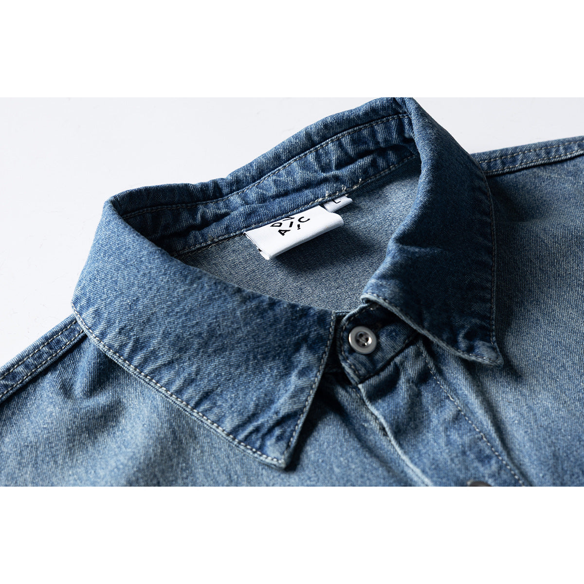 Close-up of a blue denim shirt collar, top button, and interior label.