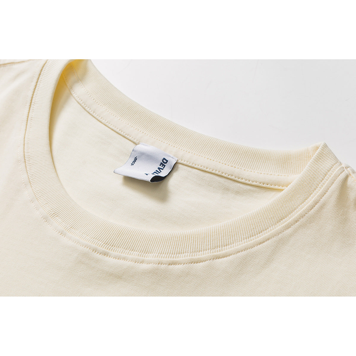Close-up of an ivory T-shirt’s ribbed crew neckline and inner brand label.