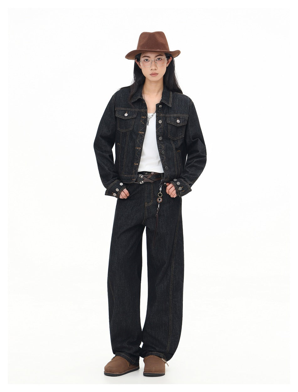 Full-length view of a model in a black denim jacket, white top, dark wide-leg jeans, brown fedora and brown shoes