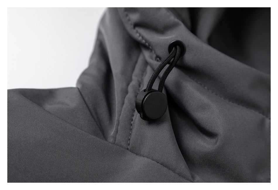 Close-up of a black cord lock and drawcord on dark gray jacket fabric.