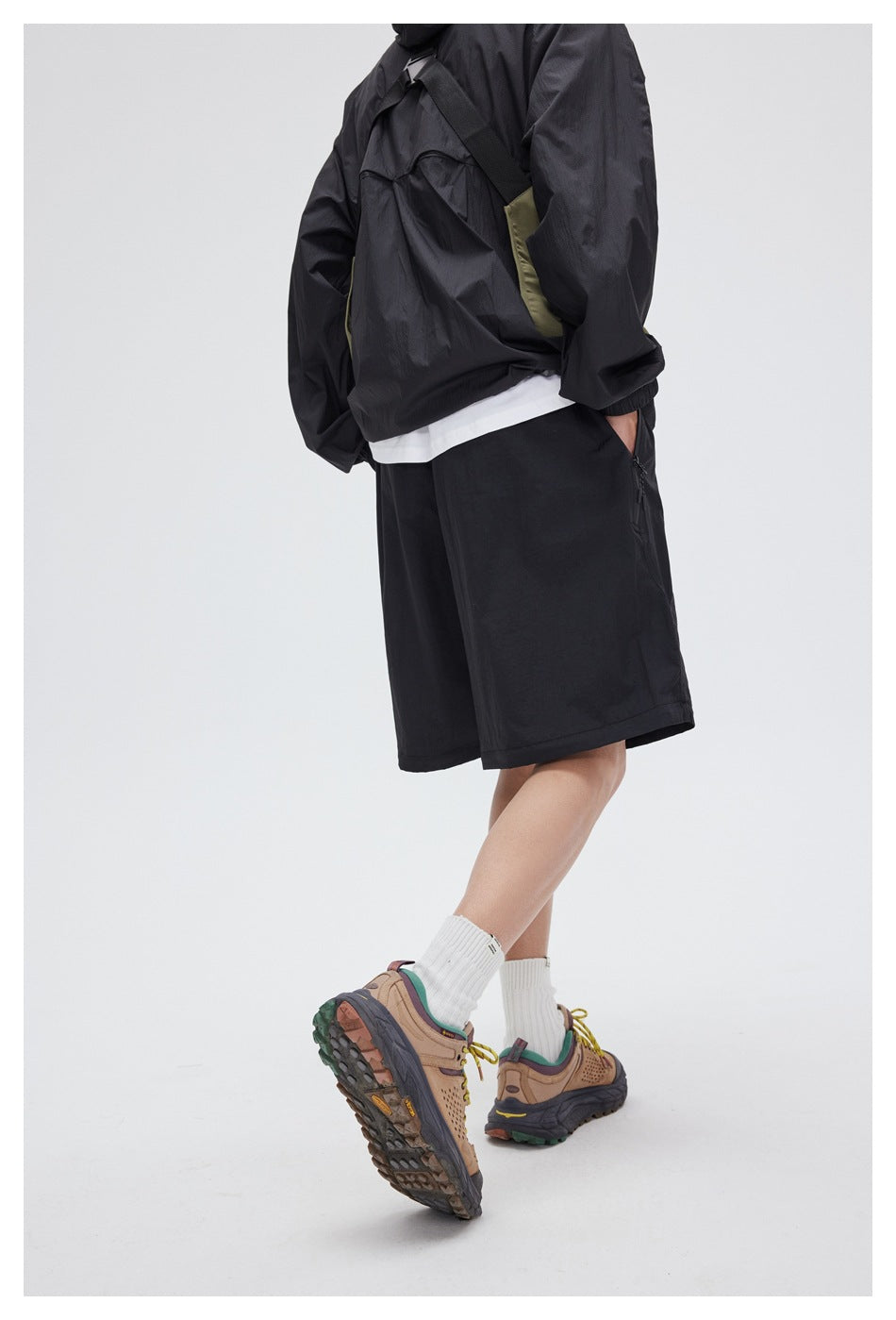 Rear-side view of a cropped model wearing black knee-length shorts with a dark jacket and hiking shoes.
