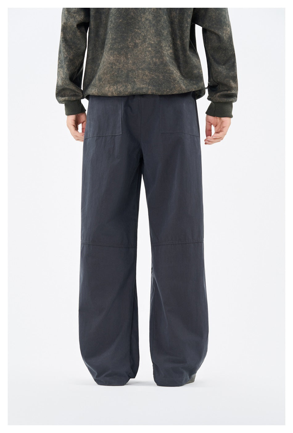 Back view of a model wearing loose navy pants with two rear patch pockets and paneled legs.