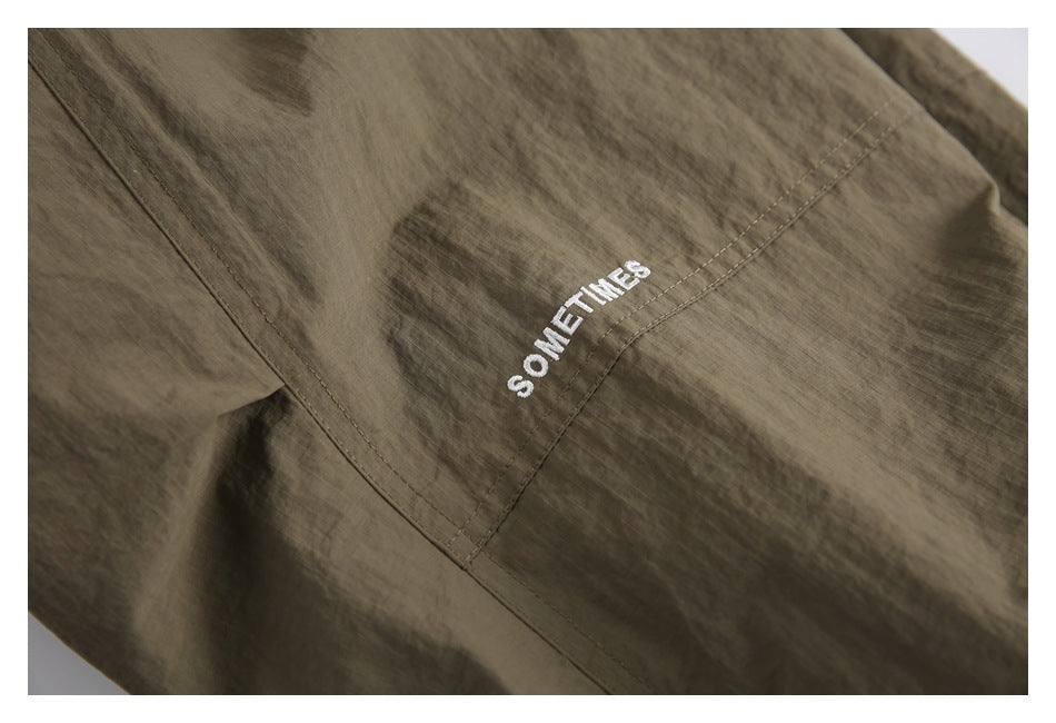 Close-up of olive-brown pants with white “SOMETIMES” embroidery.