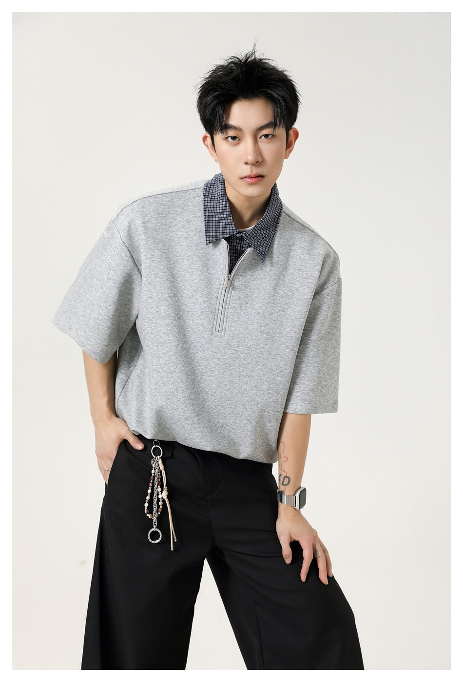 Front view of a male model wearing a light gray oversized short-sleeve top with a checked collar and short zip placket.