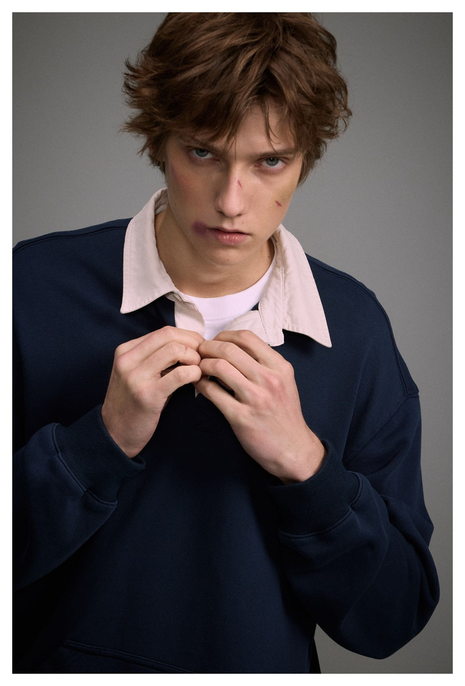 Close-up of model in navy sweatshirt with cream collar, hands at the placket, showing cuff and pocket detail