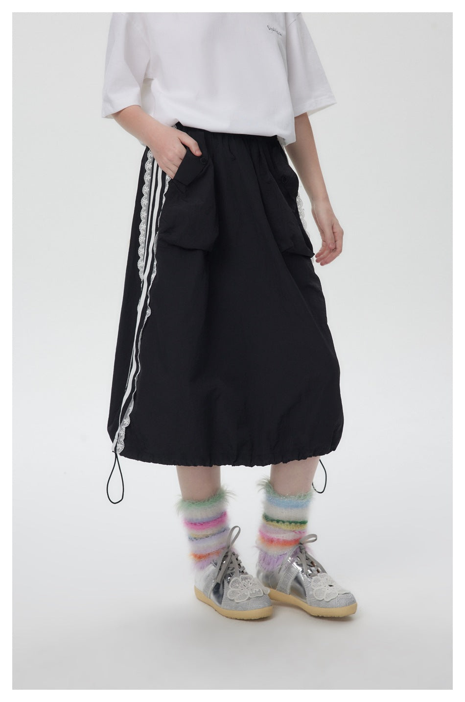 Cropped model wearing a black midi skirt with buttoned flap pockets, white striped lace trim, and drawcord hem.
